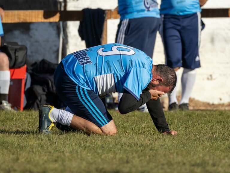 Futebolista agachado no relvado, exausto com o calor durante o treino